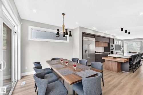 Spacious open-concept living area featuring wood-finish flooring, a contemporary chandelier, a large sliding glass door, and a horizontal transom window - 12631 52 Avenue, Edmonton, AB 
