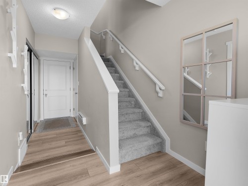 Entryway featuring wood-finish flooring, a carpeted staircase with white handrails, and a modern overhead light fixture - 49 17832 78 Street, Edmonton, AB 
