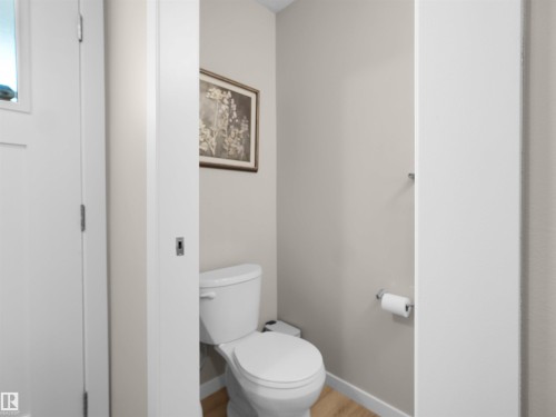 White toilet with light beige wall paint, wood-finish flooring, and a chrome towel bar - 49 17832 78 Street, Edmonton, AB 