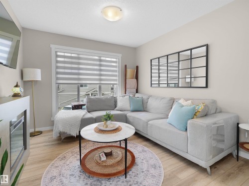 Living room featuring light wood-finish flooring, a large window with privacy blinds, and a built-in electric fireplace - 49 17832 78 Street, Edmonton, AB 