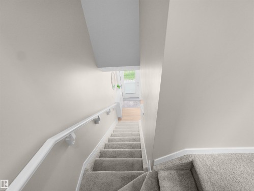 Carpeted staircase featuring a white wall-mounted handrail, neutral wall tones, white trim, and a bright entryway with a glass-paneled door - 49 17832 78 Street, Edmonton, AB 