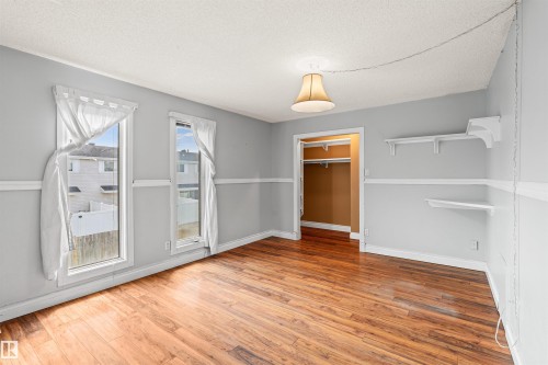 Spacious room featuring wood-finish flooring, two large windows, a built-in closet with shelving, and wall-mounted shelving - 11507 141 Avenue Nw, Edmonton, AB - Indoor Photo Showing Other Room