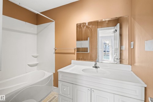 White vanity with an integrated sink and base cabinetry, complemented by a built-in tub and shower combination with white surround - 11507 141 Avenue Nw, Edmonton, AB - Indoor Photo Showing Bathroom