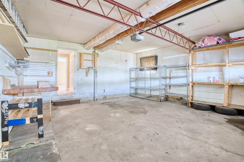 Spacious garage featuring a concrete floor, exposed ceiling joists, and multiple storage shelving units - 11507 141 Avenue Nw, Edmonton, AB - Indoor Photo Showing Garage