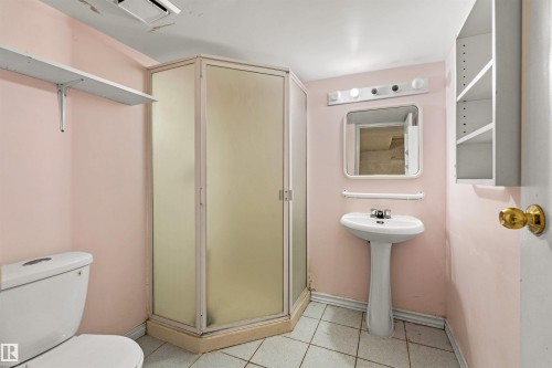 Three-quarter bathroom featuring a corner shower enclosure with frosted panels, a pedestal sink with a mirror and vanity lighting, a commode, and a wall-mounted shelving unit - 11507 141 Avenue Nw, Edmonton, AB - Indoor Photo Showing Bathroom