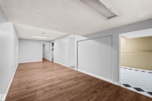 Spacious open room featuring wood-finish flooring, light gray walls, white baseboards, and overhead fluorescent lighting - 11507 141 Avenue Nw, Edmonton, AB - Indoor Photo Showing Other Room