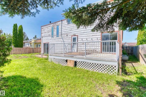 Spacious backyard featuring a slatted wood privacy fence, mature trees, and a ground-level deck with lattice skirting and metal railings - 11507 141 Avenue Nw, Edmonton, AB - Outdoor With Deck Patio Veranda