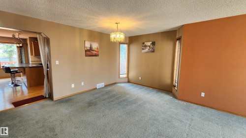 Open-concept living space featuring a chandelier, bay window, and a pass-through opening to a kitchen with hardwood-finish flooring and a breakfast bar - 2708 44A Avenue, Edmonton, AB 