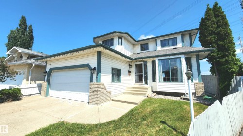 Two-story residential exterior featuring white siding with dark trim accents, an integrated garage, bay windows, concrete driveway, and front stairs with a metal railing - 2708 44A Avenue, Edmonton, AB 