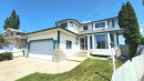 Two-story residential exterior featuring white siding with dark trim accents, an integrated garage, bay windows, concrete driveway, and front stairs with a metal railing - 2708 44A Avenue, Edmonton, AB 
