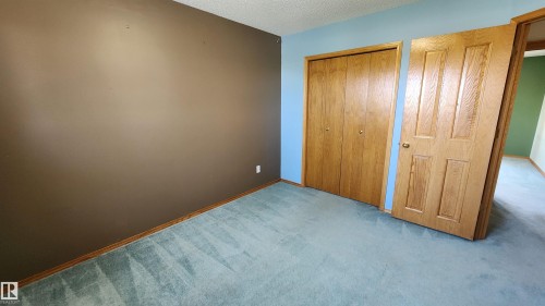 Bedroom space featuring light blue and brown painted walls, light blue carpeting, wood-paneled bi-fold closet doors, and wood-paneled interior doors - 2708 44A Avenue, Edmonton, AB 