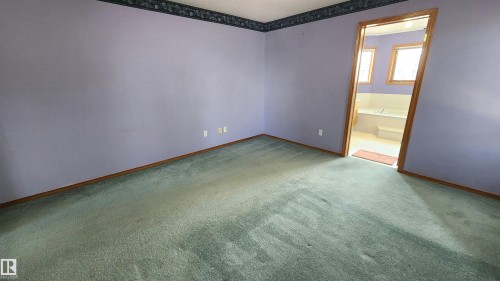 Carpeted room with a doorway opening to a bathroom featuring a built-in tub and windows - 2708 44A Avenue, Edmonton, AB 