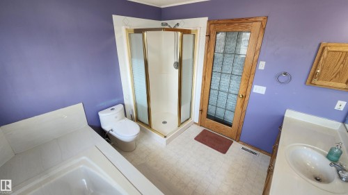Bathroom featuring a corner shower with a framed enclosure, a built-in tub, a single vanity with an integrated sink, and a wooden door with privacy glass - 2708 44A Avenue, Edmonton, AB 