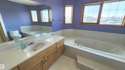 Bathroom featuring a built-in jetted tub, wood-finish vanity with an integrated sink, broad wall mirror, and multiple windows with grid patterns - 2708 44A Avenue, Edmonton, AB 