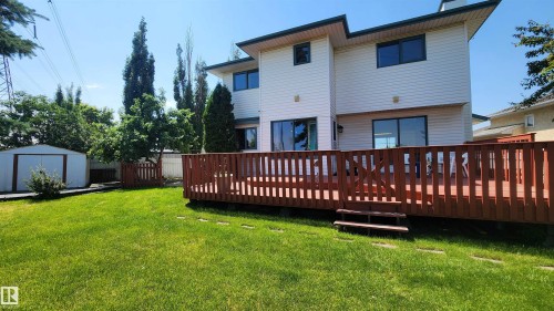 Spacious backyard featuring a substantial wood deck with railings and steps, a manicured lawn, and a white metal storage shed - 2708 44A Avenue, Edmonton, AB 