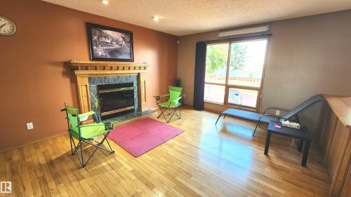 Living area featuring hardwood flooring, a fireplace with a wood-finish mantel and stone surround, and recessed ceiling lights - 2708 44A Avenue, Edmonton, AB 