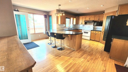 Spacious kitchen featuring wood-finish flooring, a central island with countertop seating, wood cabinetry, black countertops, and a white tile backsplash - 2708 44A Avenue, Edmonton, AB 