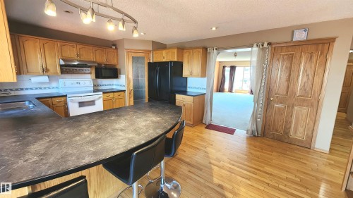 Kitchen featuring wood cabinetry, black countertops, and a peninsula with seating - 2708 44A Avenue, Edmonton, AB 