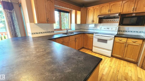Spacious kitchen featuring extensive counter space, warm wood cabinetry, a double basin sink, and a white tile backsplash - 2708 44A Avenue, Edmonton, AB 