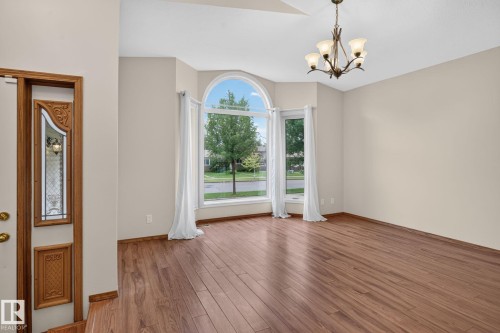 Bright living space featuring wood-finish flooring, a large arched window, and a bronze chandelier - 5612 Mcleod Road, Edmonton, AB 