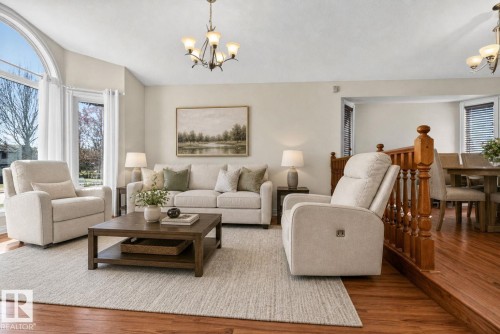 Living room featuring abundant natural light, hardwood-finish flooring, a contemporary chandelier, and an arched window - 5612 Mcleod Road, Edmonton, AB 
