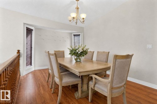 Dining area featuring wood-finish flooring, two large windows with blinds, a built-in architectural niche, and a brass chandelier - 5612 Mcleod Road, Edmonton, AB 