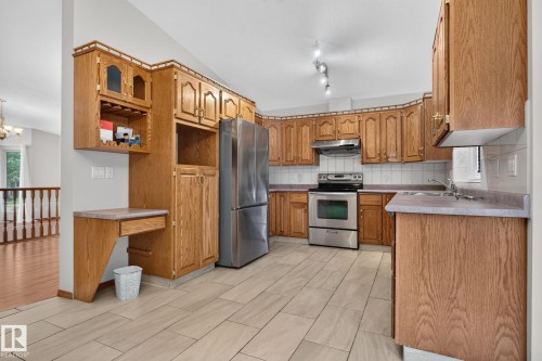 Kitchen featuring wood cabinetry, stainless steel appliances, ceramic tile flooring, a built-in desk, and track lighting - 5612 Mcleod Road, Edmonton, AB 