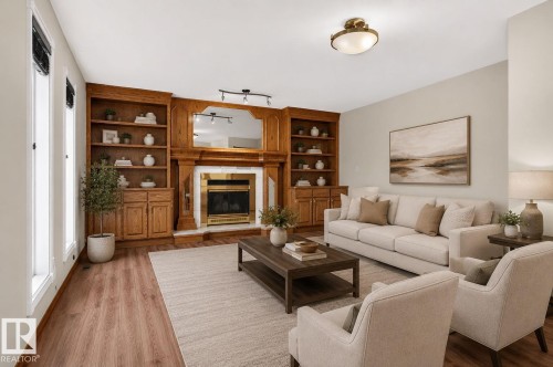 Living room featuring wood-finish flooring, a built-in fireplace with a brass-toned insert, and integrated wood cabinetry with shelving - 5612 Mcleod Road, Edmonton, AB 
