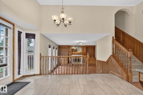 Grand entryway featuring high ceilings, light tile flooring, an elegant chandelier, and wood-paneled staircase with carpeted treads - 5612 Mcleod Road, Edmonton, AB 