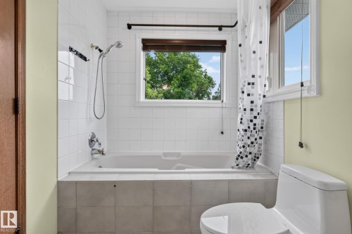 Bathroom featuring a white subway tile surround, a built-in tub with chrome fixtures, and a window with a wood-finish blind - 5612 Mcleod Road, Edmonton, AB 