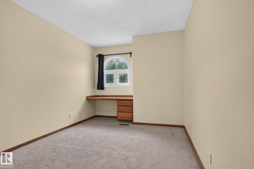 Room featuring an arched window, built-in wooden desk, and neutral-toned carpeting - 5612 Mcleod Road, Edmonton, AB 