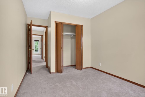 Carpeted interior room featuring neutral wall paint, wood-finish bi-fold closet doors, and wood-finish trim - 5612 Mcleod Road, Edmonton, AB 