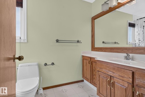 Bathroom featuring a wood-finish vanity with a white countertop and integrated sink, a large framed mirror, and light-colored walls - 5612 Mcleod Road, Edmonton, AB 
