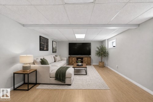 Spacious recreation room featuring light wood-finish flooring, light grey painted walls, and a drop-tile ceiling with recessed lighting - 5612 Mcleod Road, Edmonton, AB 
