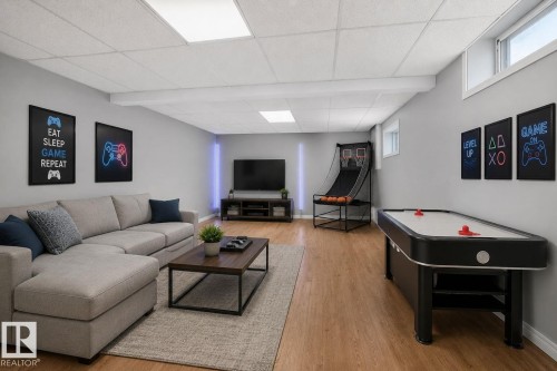 Spacious entertainment room featuring recessed lighting, a drop ceiling, wood-finish flooring, and light gray walls - 5612 Mcleod Road, Edmonton, AB 