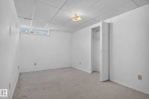 Carpeted room featuring a drop ceiling, a horizontal window, and a bi-fold door closet - 5612 Mcleod Road, Edmonton, AB 