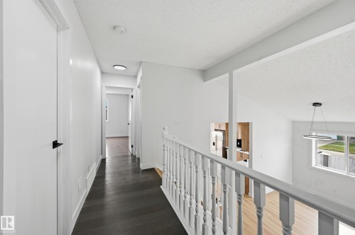 Upper-level hallway featuring dark wood-finish flooring, white walls, and contemporary flush-mount lighting - 631 Jenner Cove Cove, Edmonton, AB 