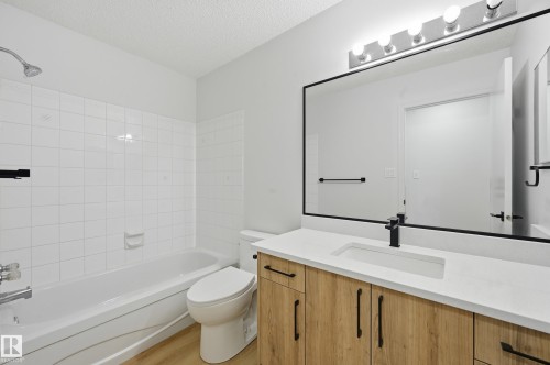 Bathroom featuring a white bathtub with subway tile surround, wood-finish vanity with a white countertop, integrated rectangular sink, and matte black fixtures - 631 Jenner Cove Cove, Edmonton, AB 