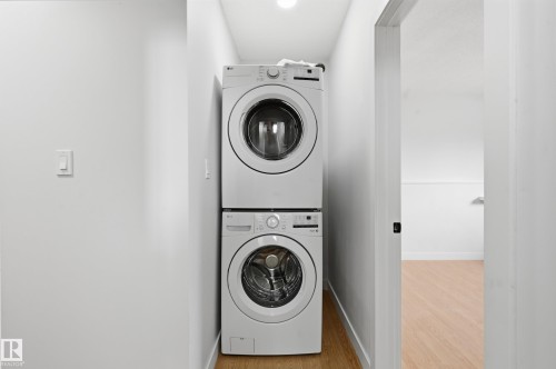 Dedicated laundry area featuring stacked front-load washing machine and dryer, light wood-finish flooring, and white walls - 631 Jenner Cove Cove, Edmonton, AB 