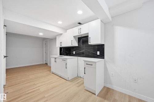 Compact kitchen area featuring white cabinetry, a black backsplash with white veining, and light wood-finish flooring - 631 Jenner Cove Cove, Edmonton, AB 
