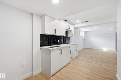 Modern kitchenette with white cabinetry, black hardware, black and white veined backsplash, undermount sink, and matte black faucet - 631 Jenner Cove Cove, Edmonton, AB 