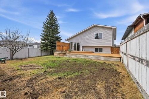 Expansive backyard featuring a multi-level wood deck, mature evergreen tree, wood fencing, and sliding glass door access to the residence - 631 Jenner Cove Cove, Edmonton, AB 