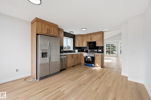 Kitchen featuring wood-finish cabinetry, stainless steel appliances, dark marble-look countertops, and a matching backsplash - 631 Jenner Cove Cove, Edmonton, AB 