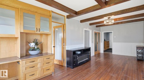 Open-concept interior featuring wood-finish flooring, exposed ceiling beams, and a built-in light wood cabinet system with frosted glass uppers and a dark countertop - 10115 104 Street, Westlock, AB 