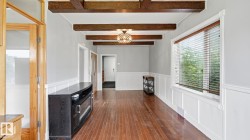 Spacious interior with wood-finish flooring, exposed ceiling beams, wainscoting, and a large window with blinds - 