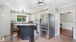 Kitchen featuring a central island with a light-toned countertop, white cabinetry with clear-fronted upper doors, stainless steel appliances, and tile flooring - 