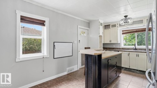 Kitchen featuring a central island with an extended breakfast bar, cream-colored cabinetry, stainless steel refrigerator, dark countertops, and a decorative ceiling light fixture - 10115 104 Street, Westlock, AB 