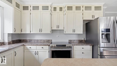 Kitchen featuring extensive cream-colored cabinetry with dark hardware, stone-look countertops, and a built-in stainless steel range - 10115 104 Street, Westlock, AB 