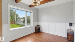 Interior room featuring hardwood flooring, white wainscoting, light gray walls, a large multi-pane window, and exposed ceiling beams - 