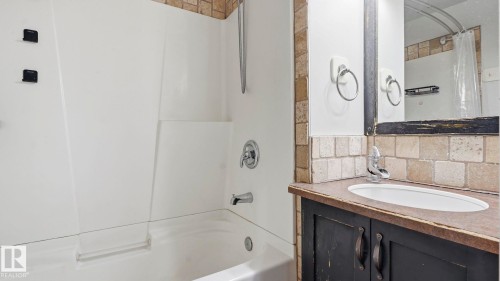 Bathroom featuring a white bathtub, integrated shower, tiled backsplash, dark wood-finish vanity, and an oval undermount sink - 10115 104 Street, Westlock, AB 